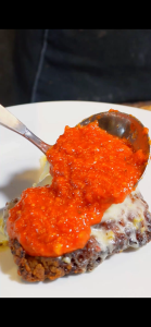 pouring homemade marinara sauce over chicken parm