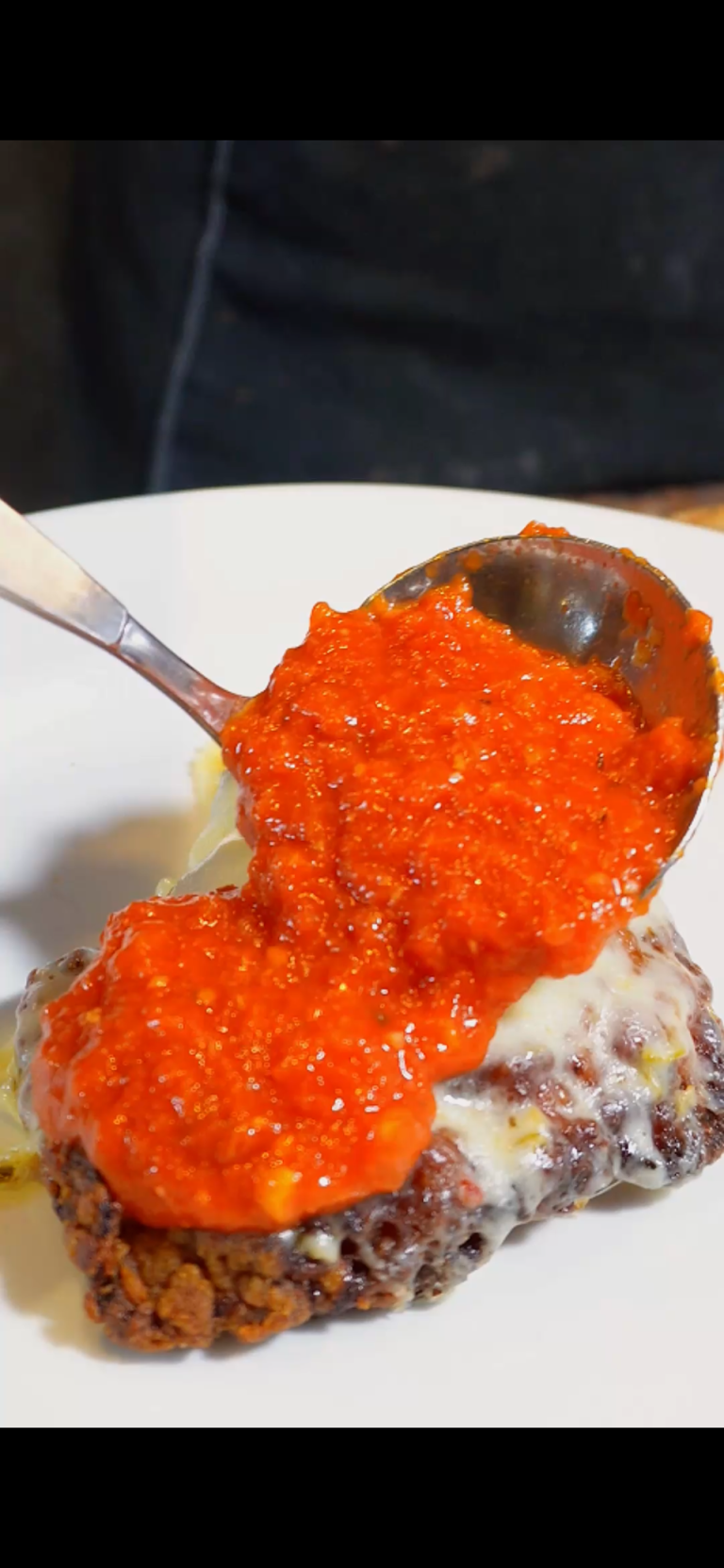 pouring homemade marinara sauce over chicken parm