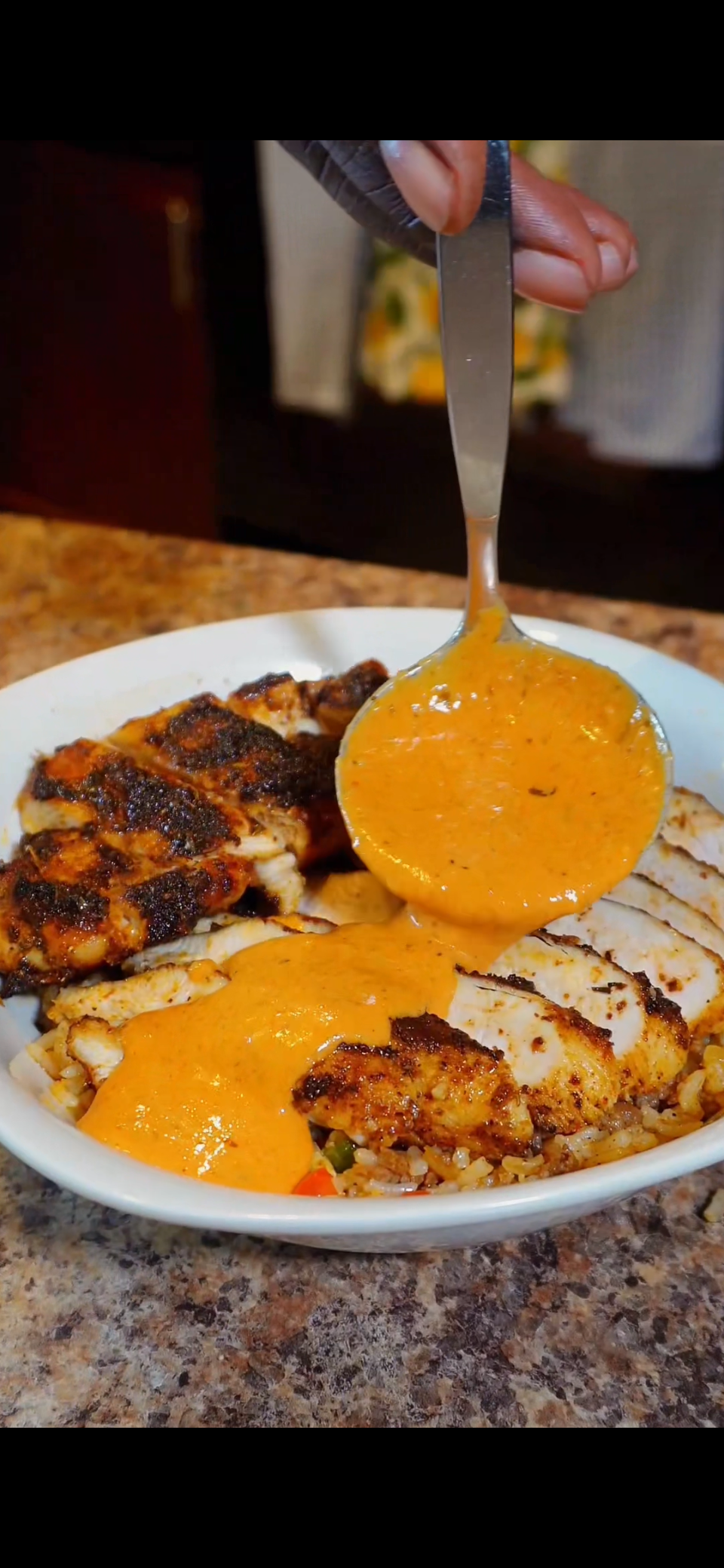 blackened chicken with dirty rice and cream sauce being poured