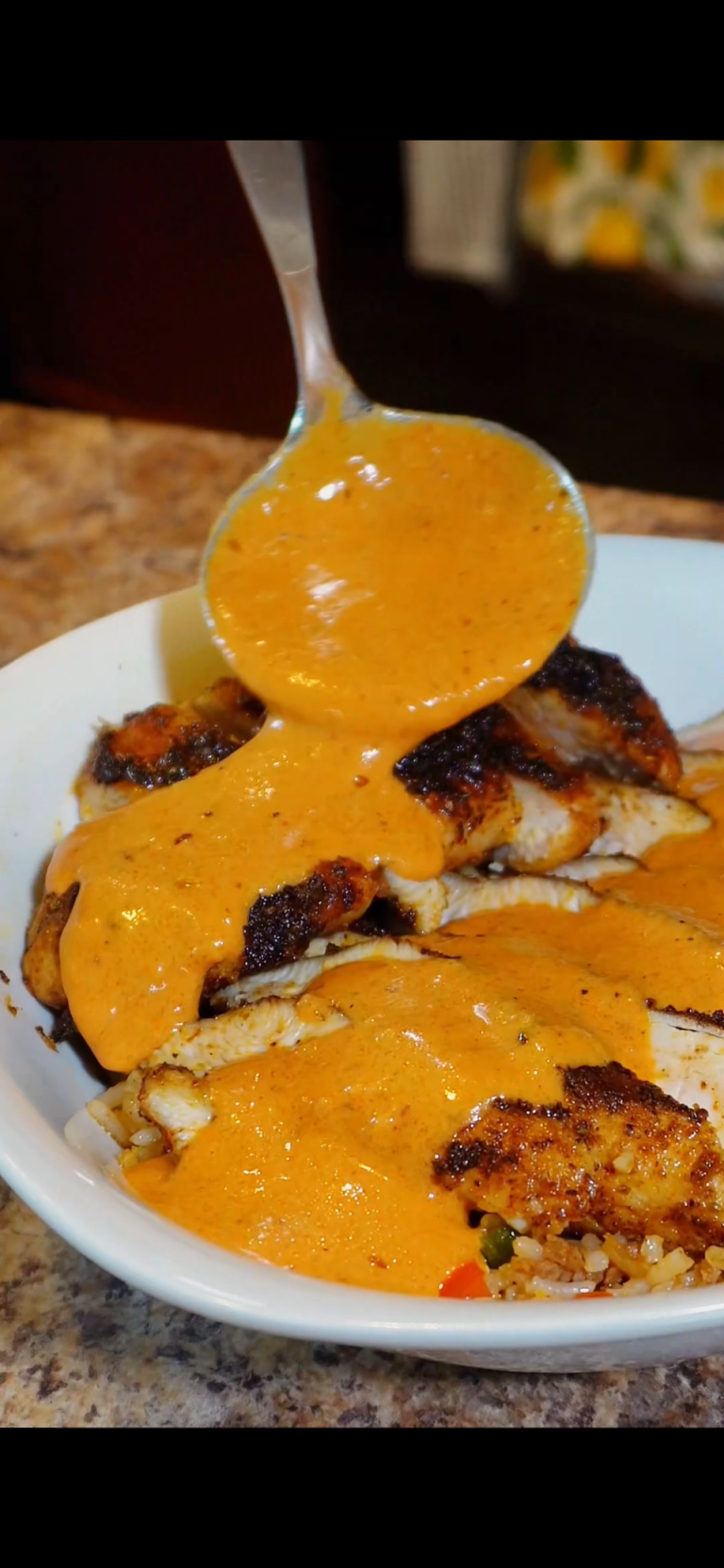 blackened chicken with dirty rice and cream sauce being poured
