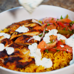 chicken shawarma in a bowl over rice with a salad and garlic sauce on top