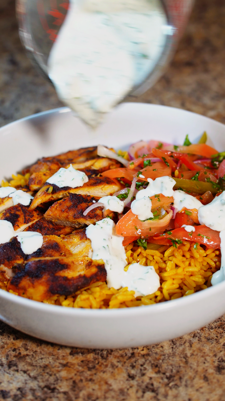 chicken shawarma in a bowl over rice with a salad and garlic sauce on top